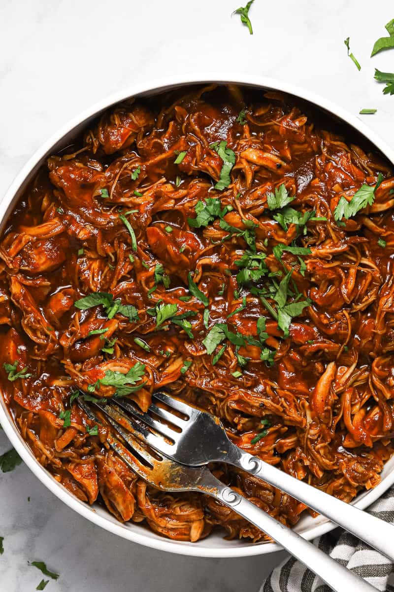 White bowl filled with shredded barbecue chicken garnished with chopped cilantro