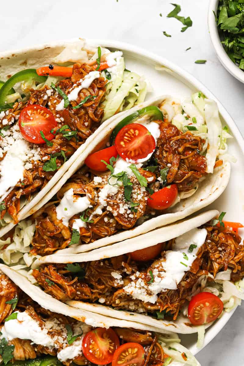 White plate with shredded BBQ chicken tacos garnished with fresh cilantro