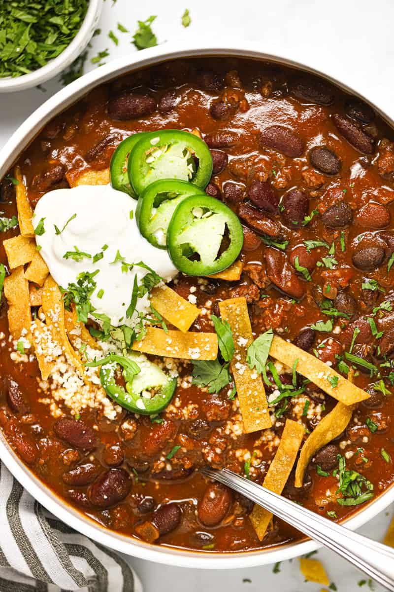 White bowl filled with beer chili garnished with cilantro and tortilla strips