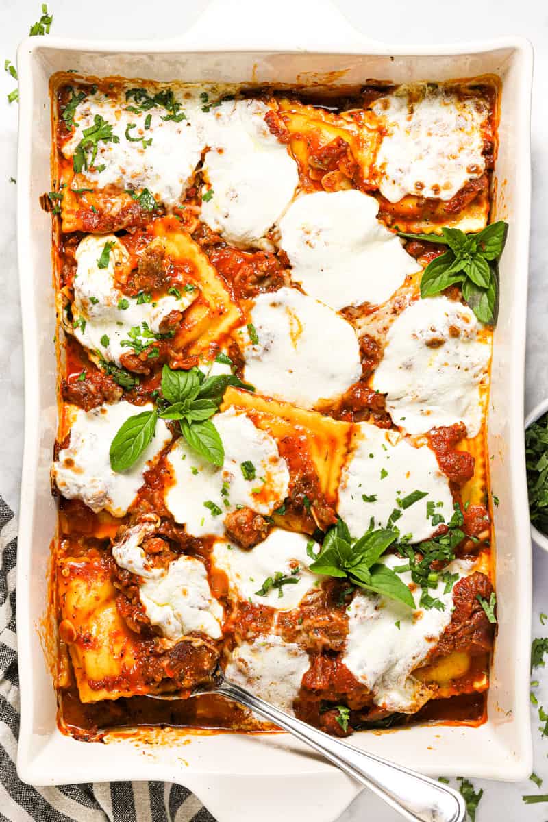 Large white baking dish filled with ravioli sausage and cheese lasagna garnished with fresh basil