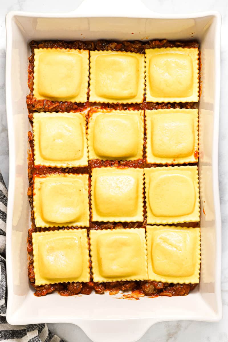 Large white pan filled with ingredients to make ravioli lasagna