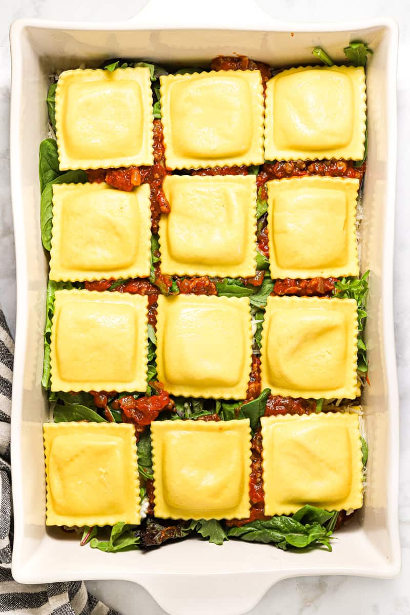 Large white pan filled with ingredients to make ravioli lasagna