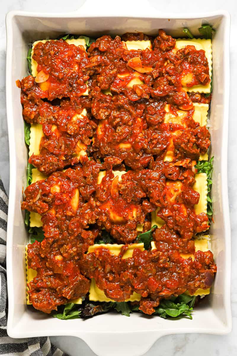 Large white pan filled with ingredients to make ravioli lasagna
