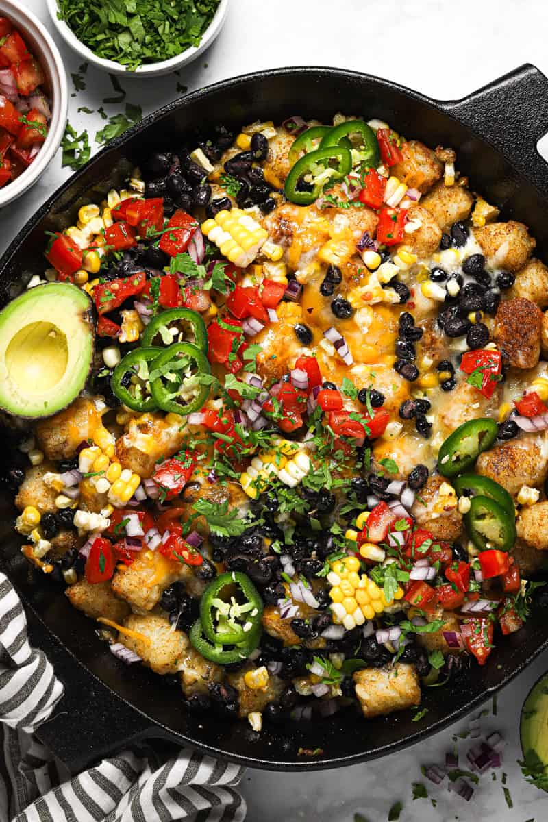 Large cast iron skillet with loaded vegetarian totchos garnished with cilantro