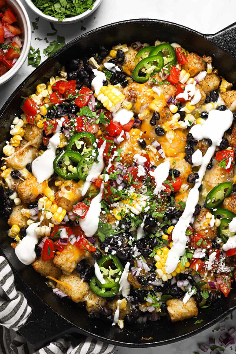 Large cast iron skillet with loaded vegetarian totchos garnished with cilantro and sour cream 