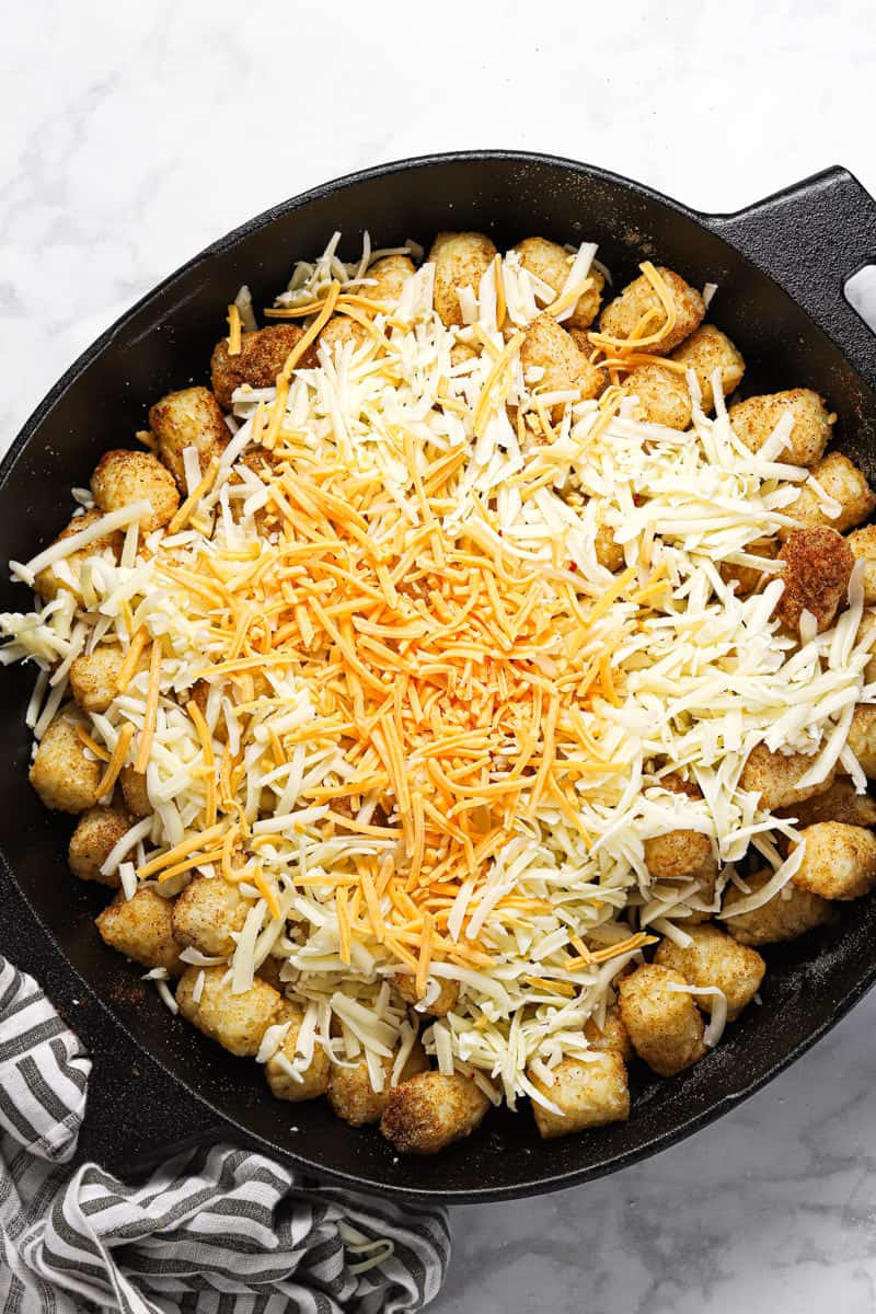 Tater tots in a cast iron skillet topped with shredded cheese
