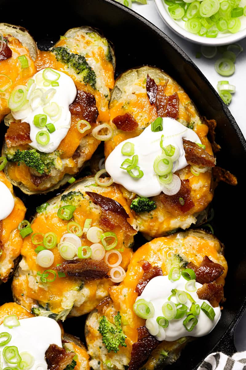 Close up shot of a large cast iron pan filled with twice baked potatoes garnished with sour cream and sliced green onion