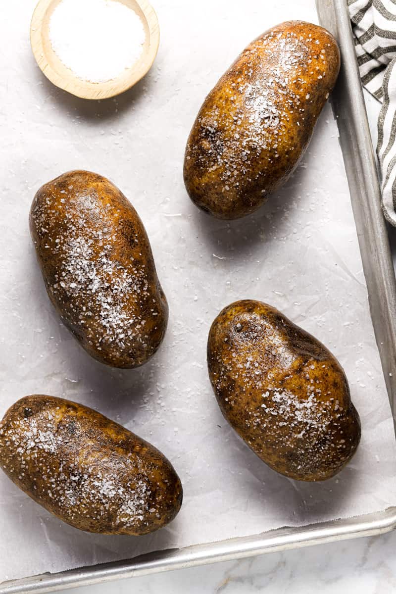 Russet potatoes on a parchment lined baking sheet seasoned with Kosher salt