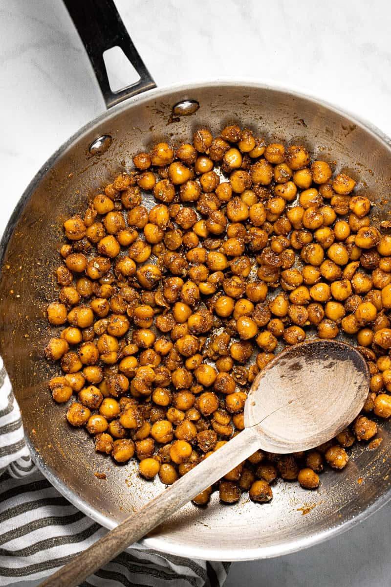 Metal pan filled with sauteed chickpeas and a wooden spoon