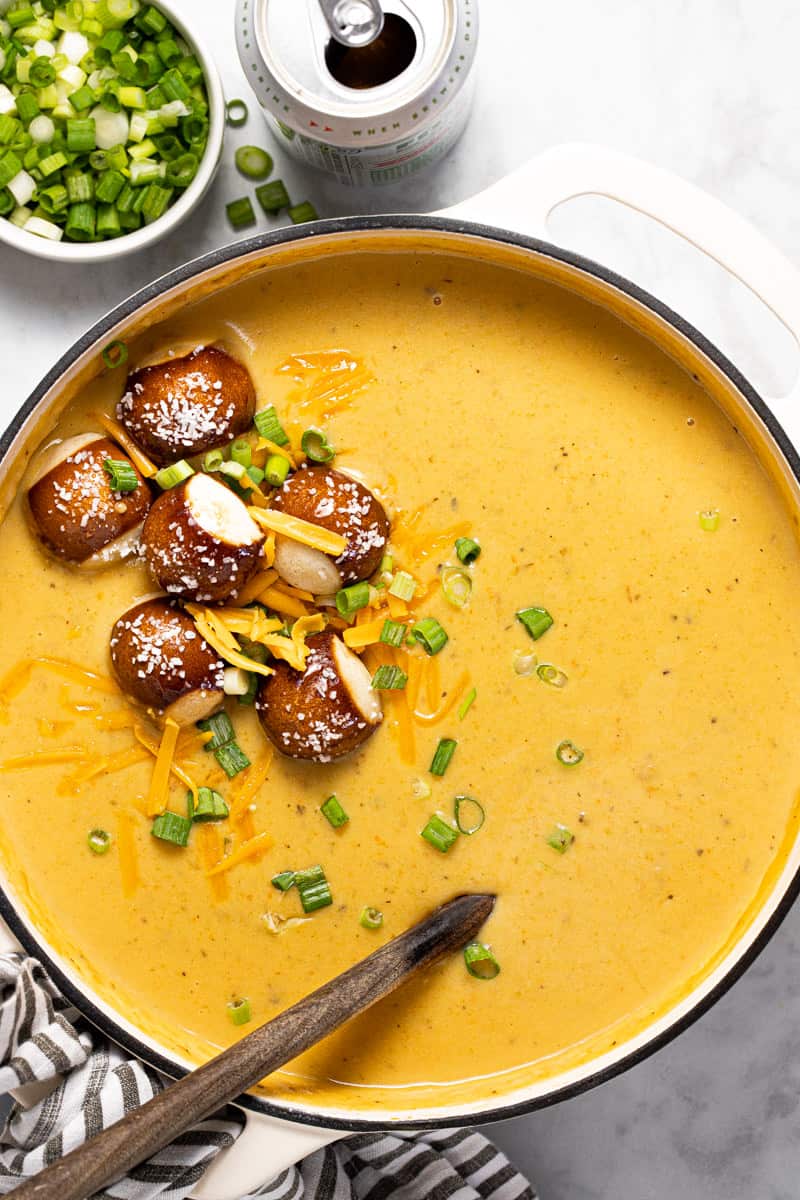 White pot filled with beer cheese soup topped with pretzel bites and green onions