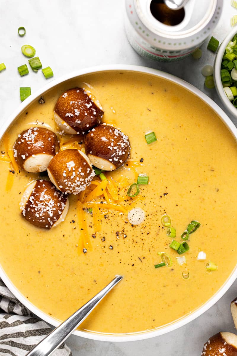 White bowl filled with beer cheese soup topped with pretzel bites and green onions