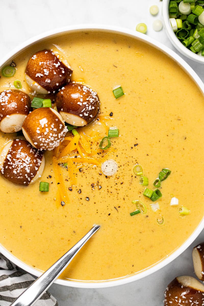 White bowl filled with beer cheese soup topped with pretzel bites and green onions