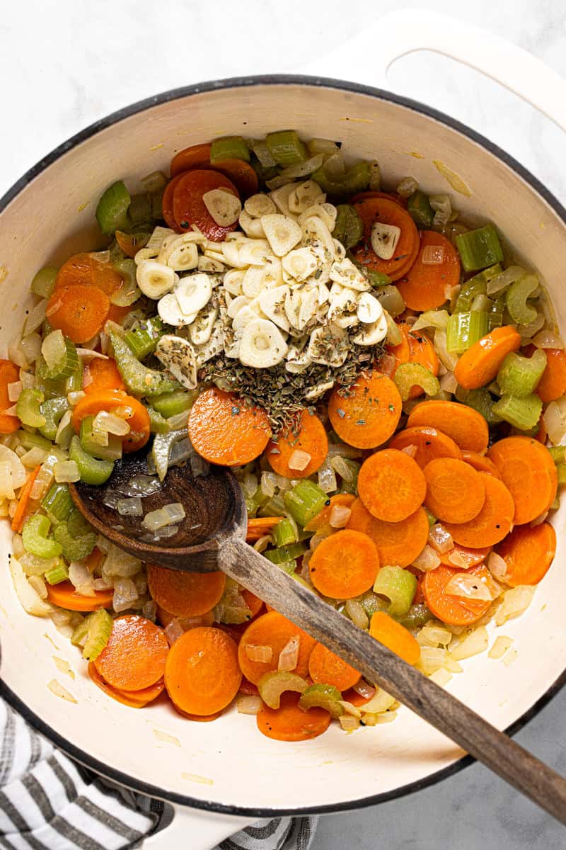 Large white pot with sautéed carrots celery onion with garlic and herbs