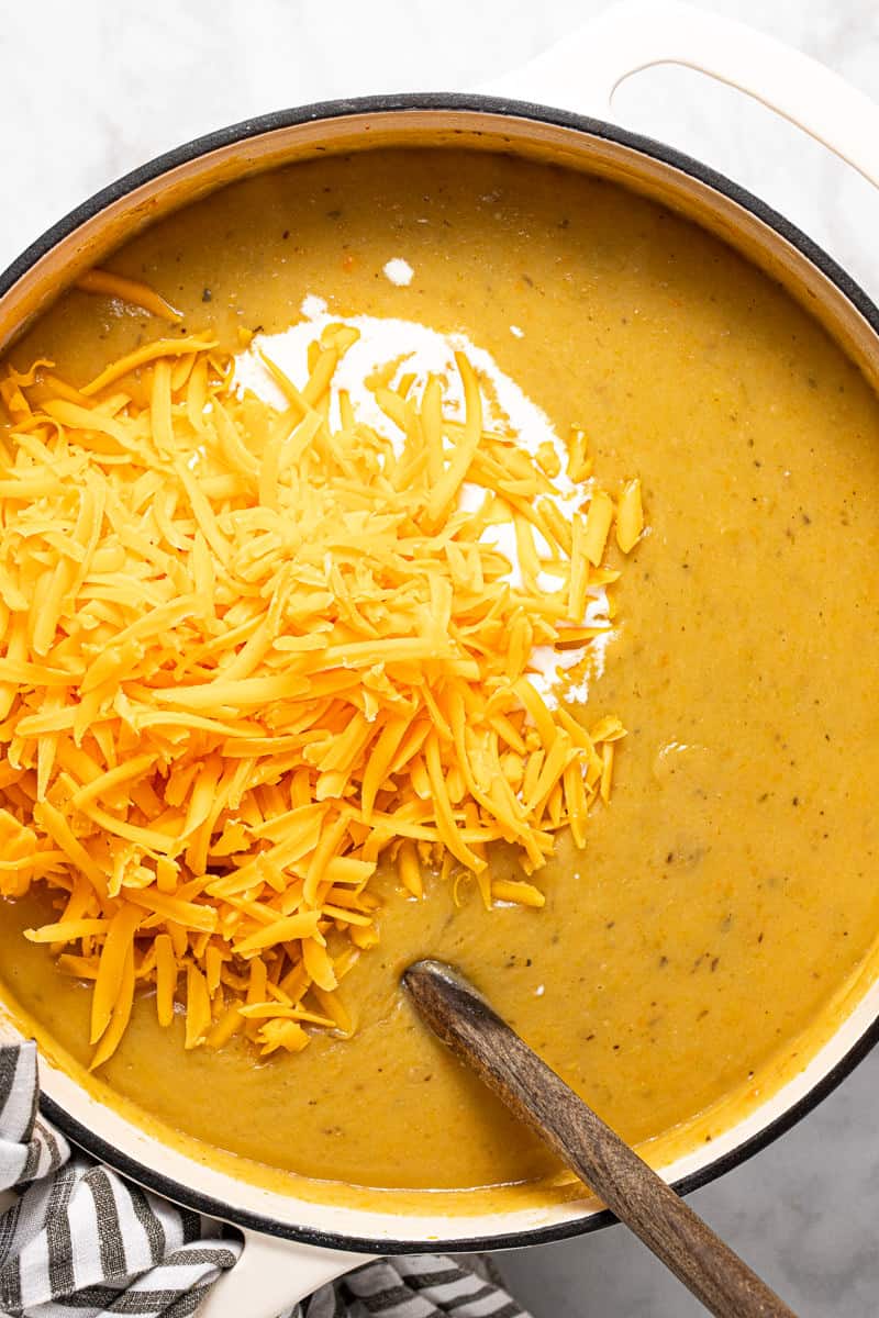 Shredded cheese and heavy cream being added to beer cheese soup in a large pot