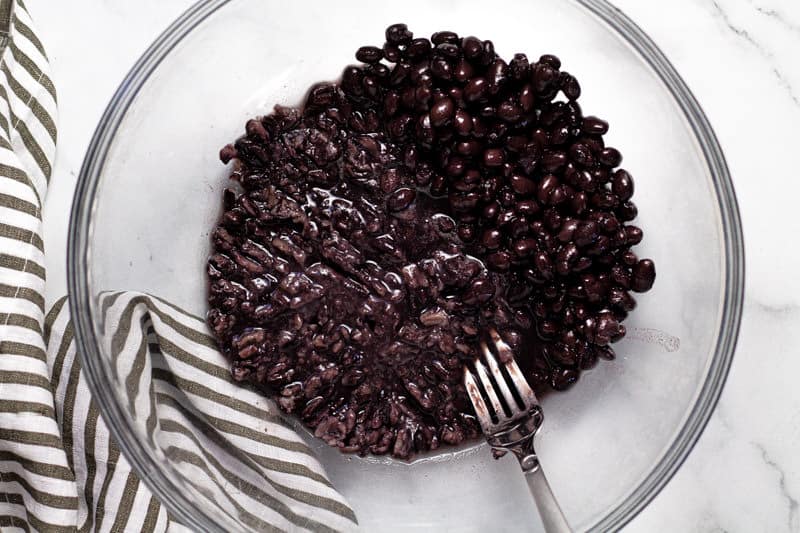 Glass bowl with black beans that are being mashed with a fork 