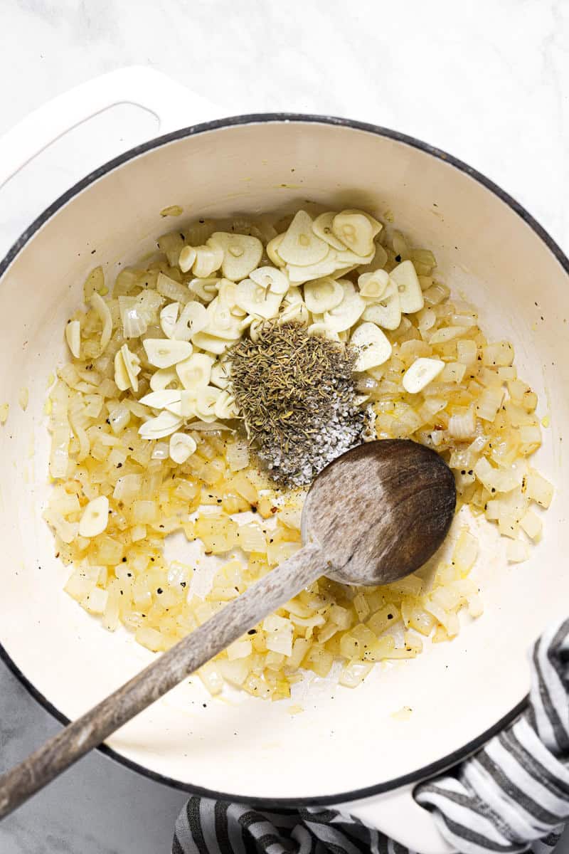 Large white pot with sautéed onion fresh sliced garlic and dried herbs