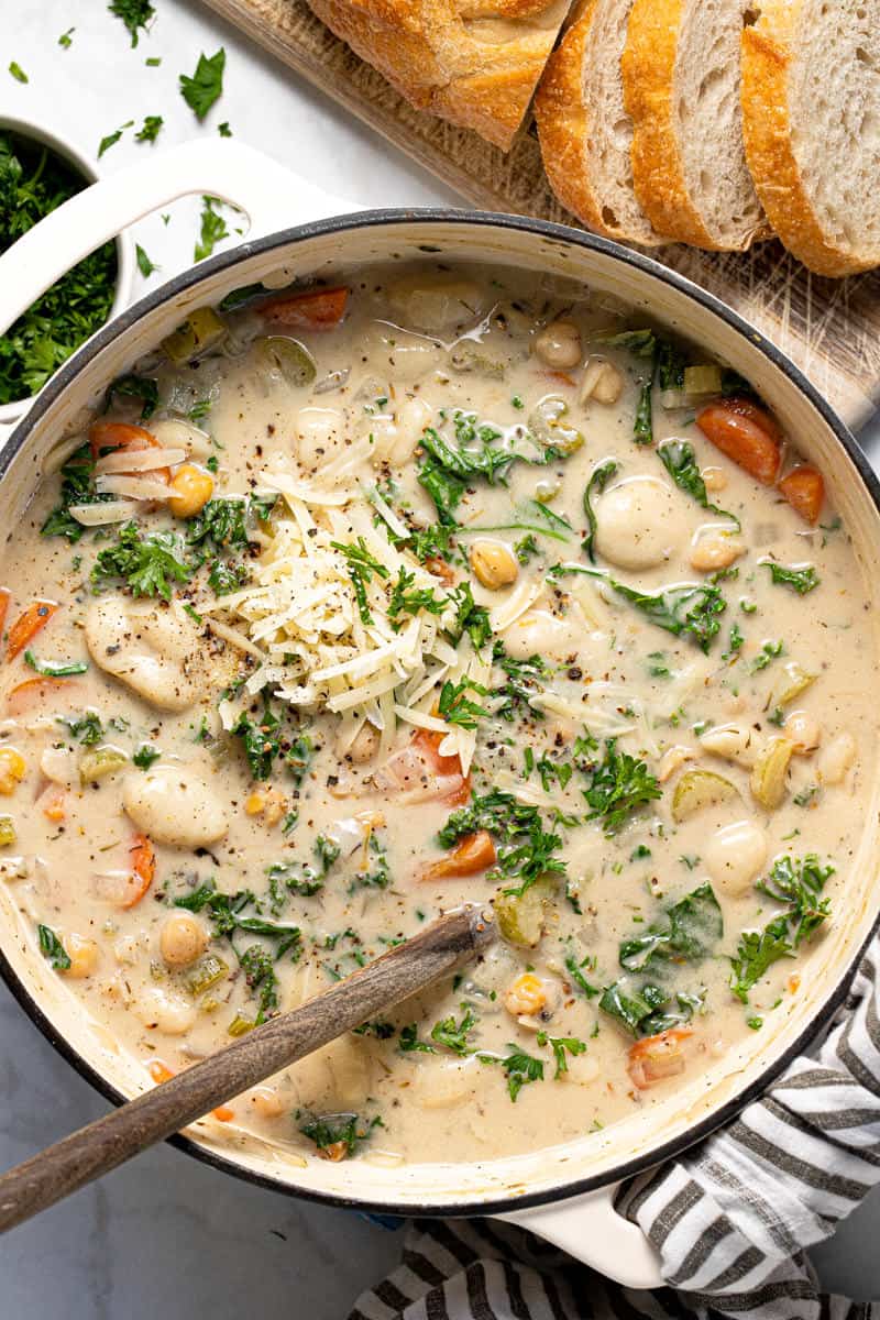 Large white pot filled with creamy chickpea gnocchi soup garnished with fresh parsley 