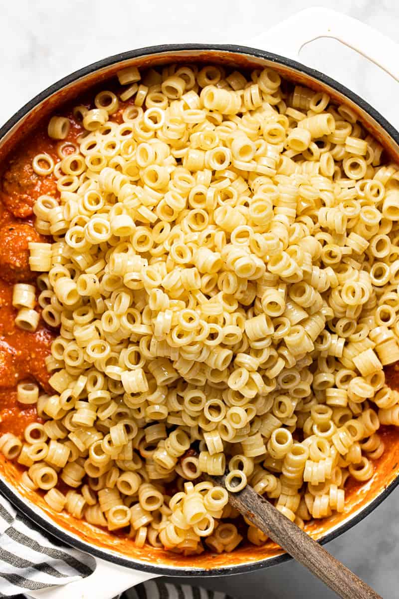 Ring noodles being added to cheesy tomato sauce and meatballs