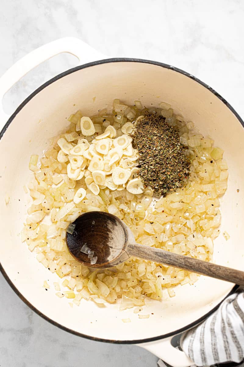 Large white pot with sautéed onions sliced garlic and dried herbs