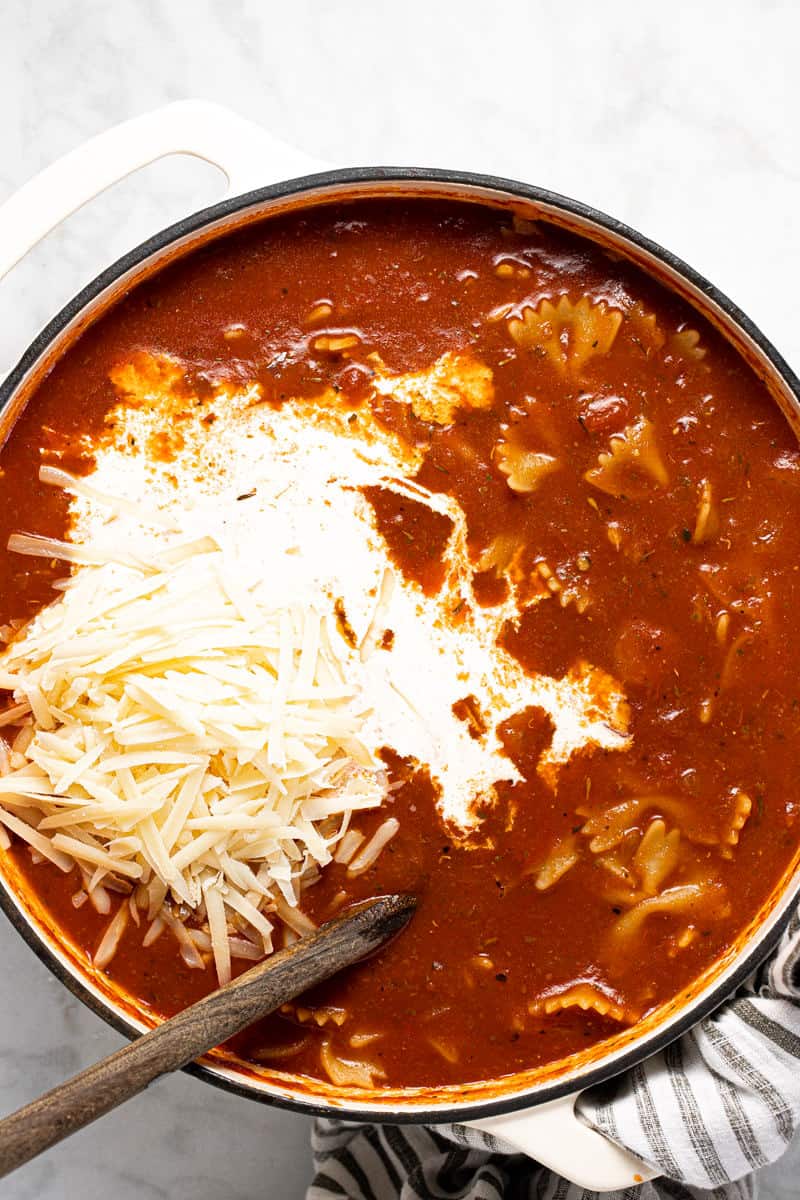 White pot filled with lasagna soup with Parmesan and cream being added