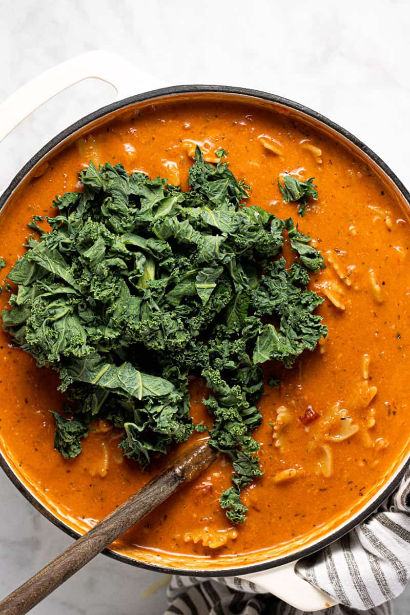 Lasagna soup in a pot with chopped kale being added 