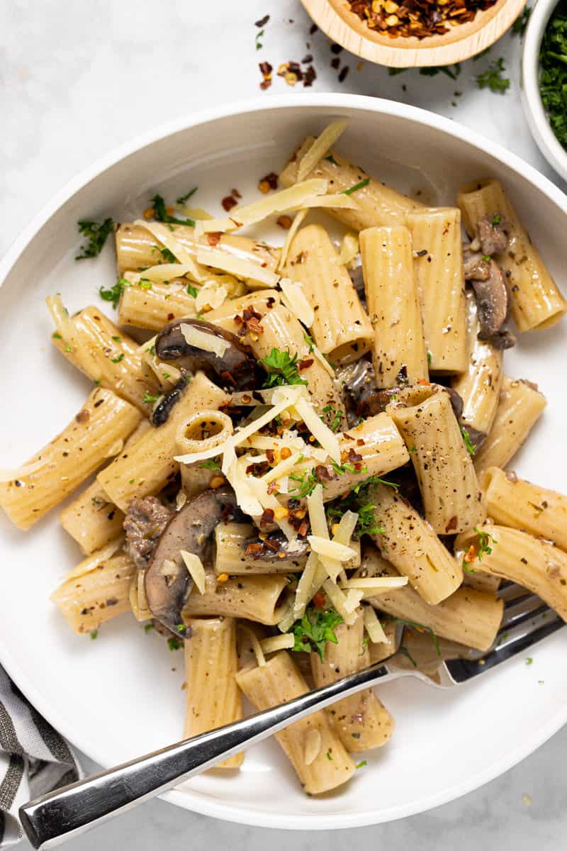 White bowl filled with creamy sausage and mushroom pasta garnished with Parmesan and red pepper flakes