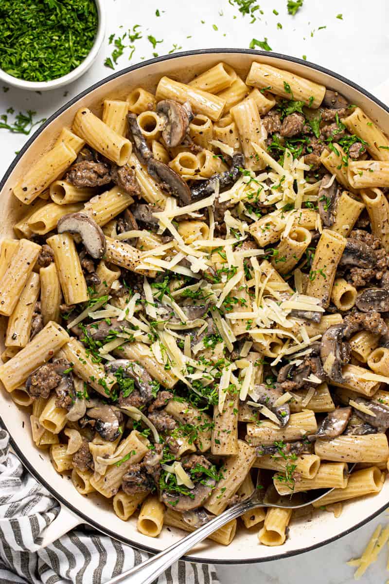 Large pan filled with creamy sausage and mushroom pasta garnished with Parmesan and red pepper flakes
