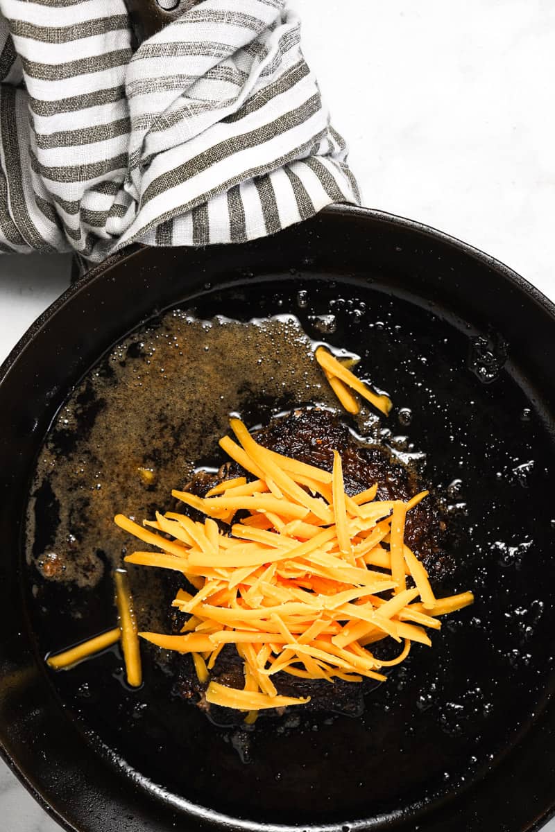 Cast iron skillet with homemade smash burger in it topped with shredded cheese