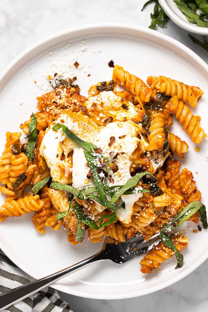 White plate filled with no boil baked pasta garnished with Parmesan and basil 