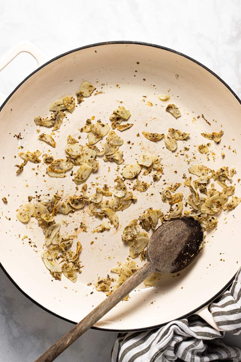 Large white pan with sautéed garlic and herbs in it