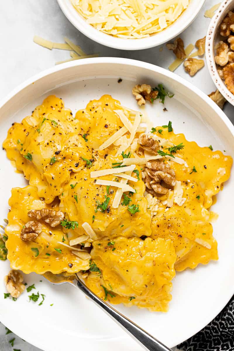 Large white bowl with ravioli tossed in squash cream sauce topped with Parmesan and walnuts