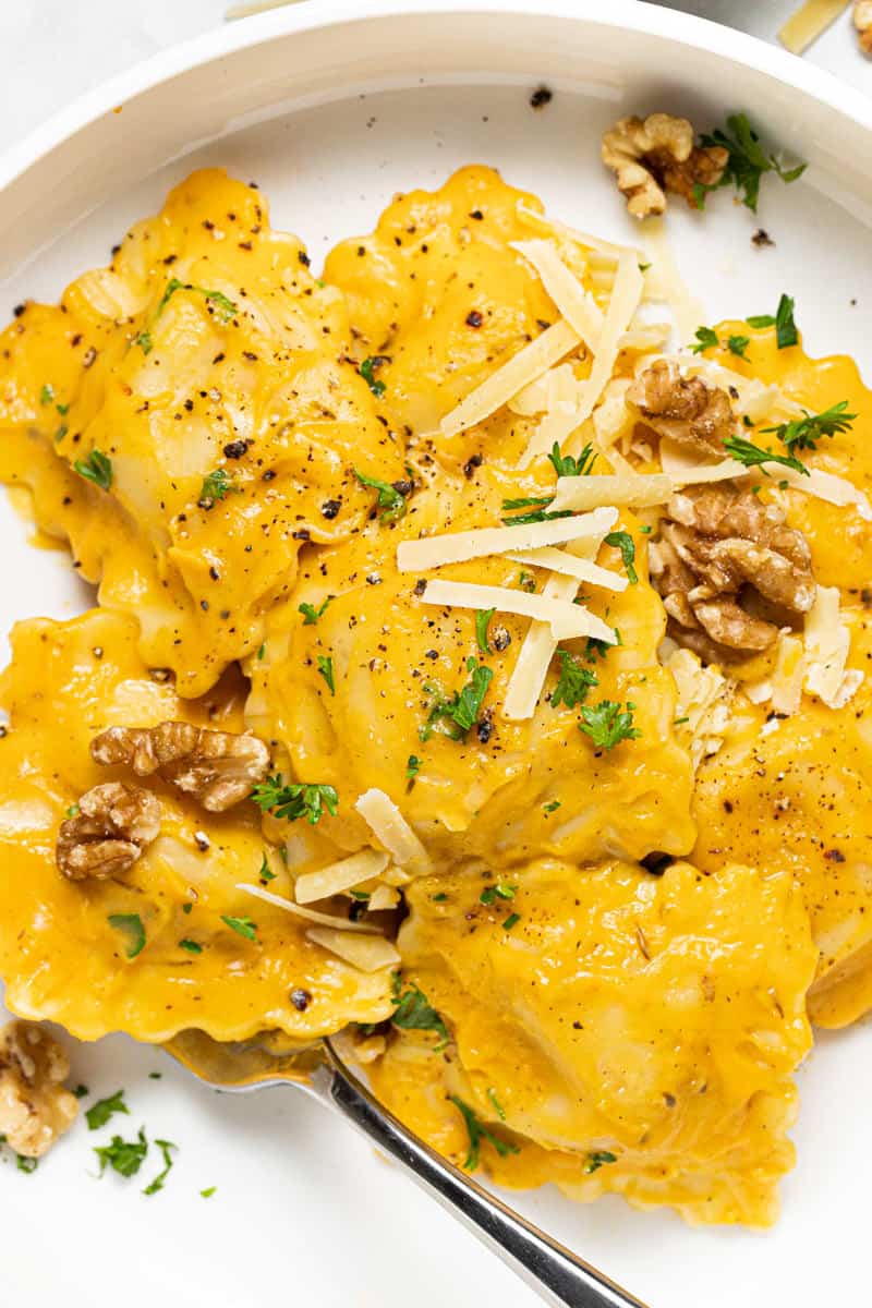 Large white bowl with ravioli tossed in squash cream sauce topped with Parmesan and walnuts
