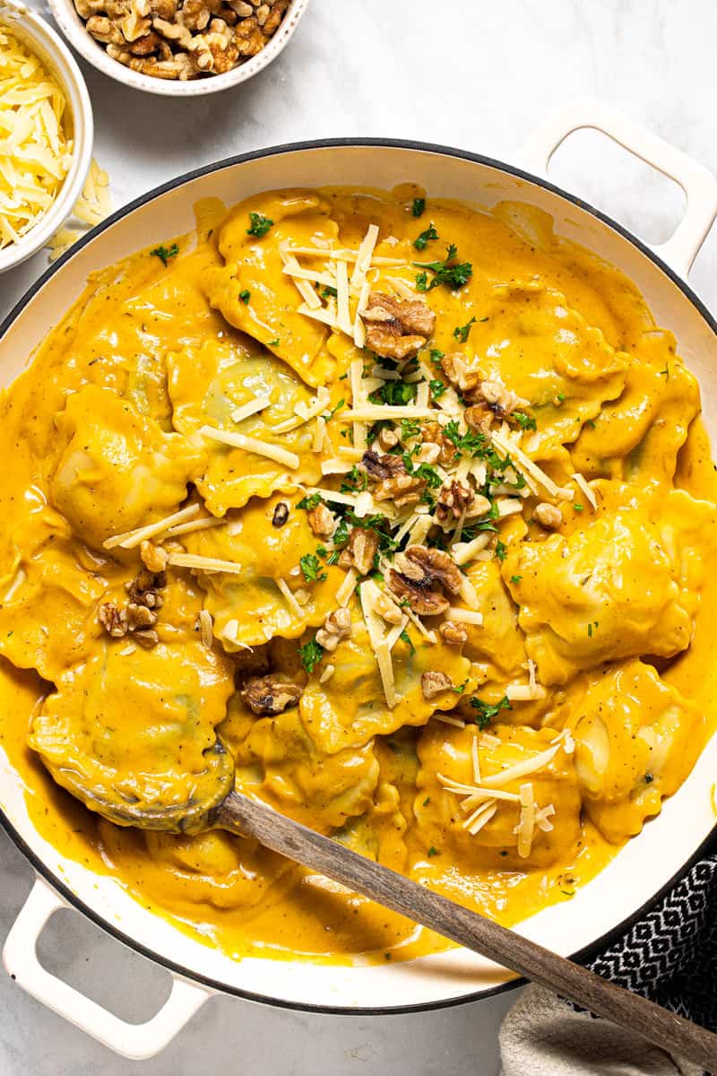 Large white pot filled with ravioli tossed in squash cream sauce topped with Parmesan and walnuts