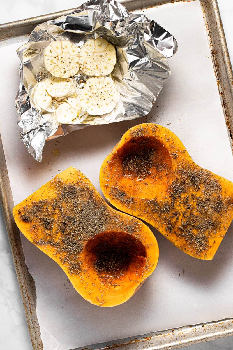 Baking sheet with halved squash and garlic ready to roast