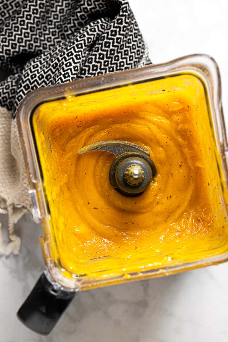 A blender pitcher filled with creamy squash and garlic sauce