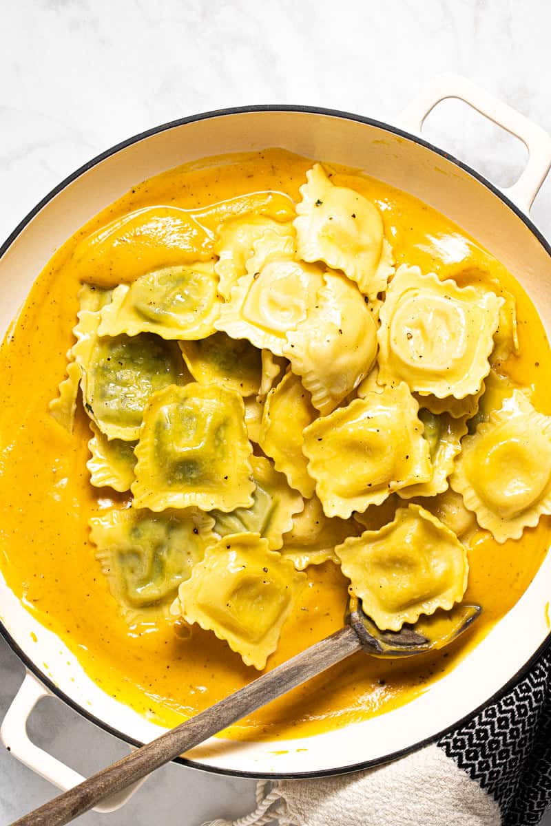 Ravioli being added to a large pot of roasted squash cream sauce