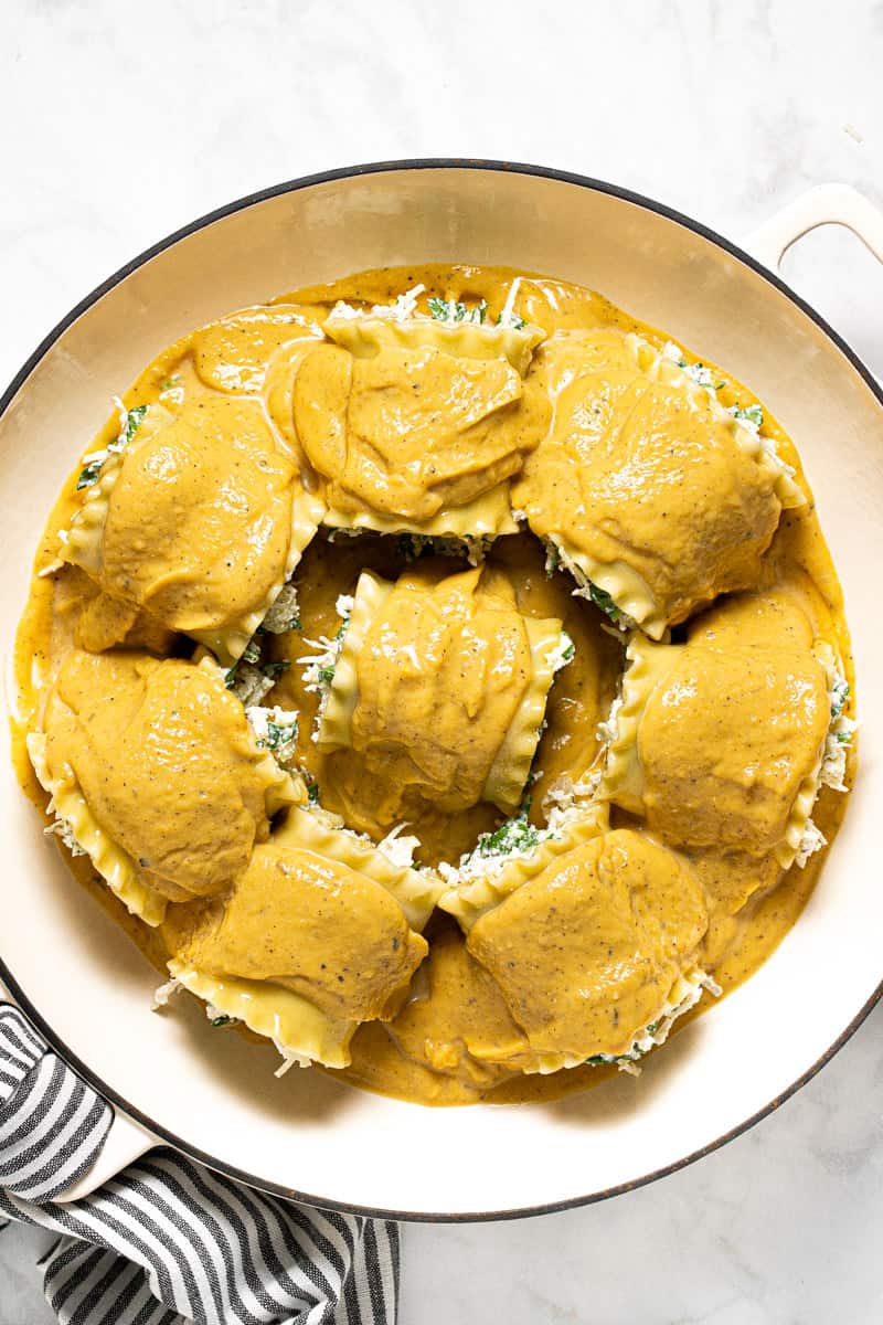 Squash lasagna roll ups in a white pan topped with creamy squash sauce