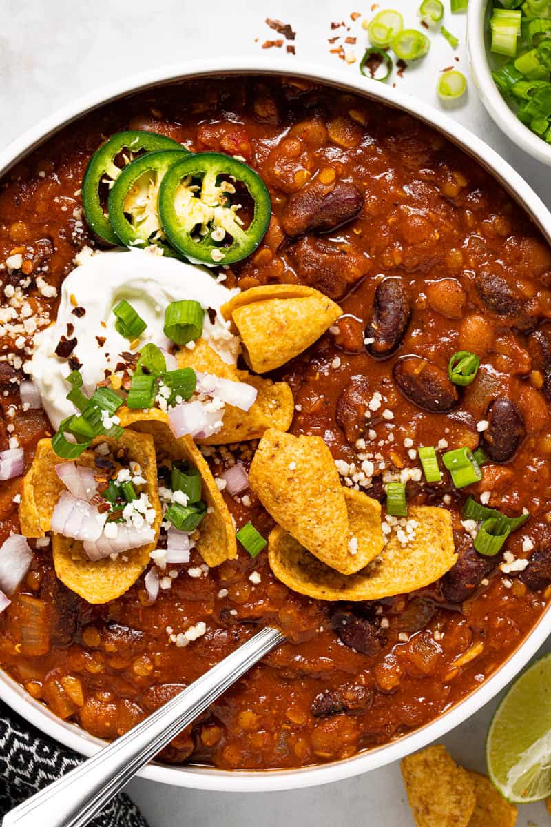 Large white bowl filled with vegan chili garnished with green onion and Fritos