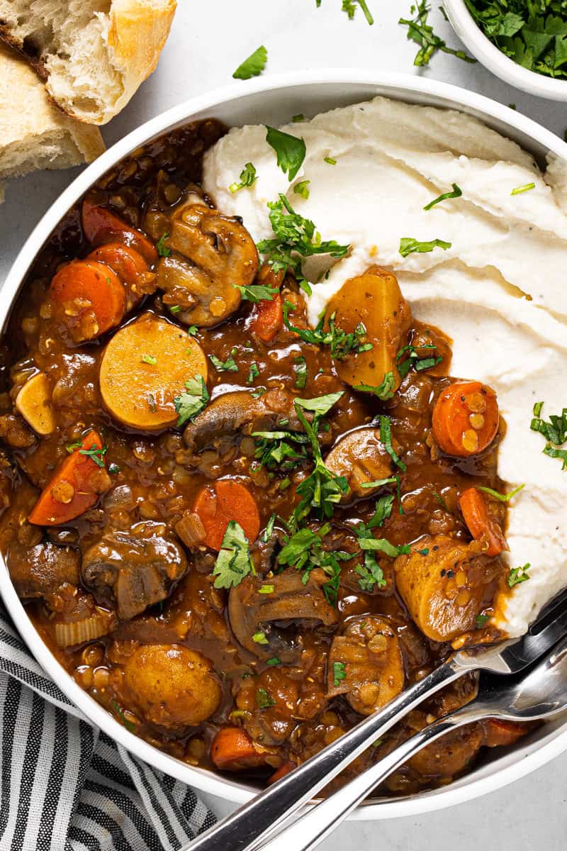 Large white bowl filled with vegetable stew recipe and mashed potatoes garnished with fresh parsley 