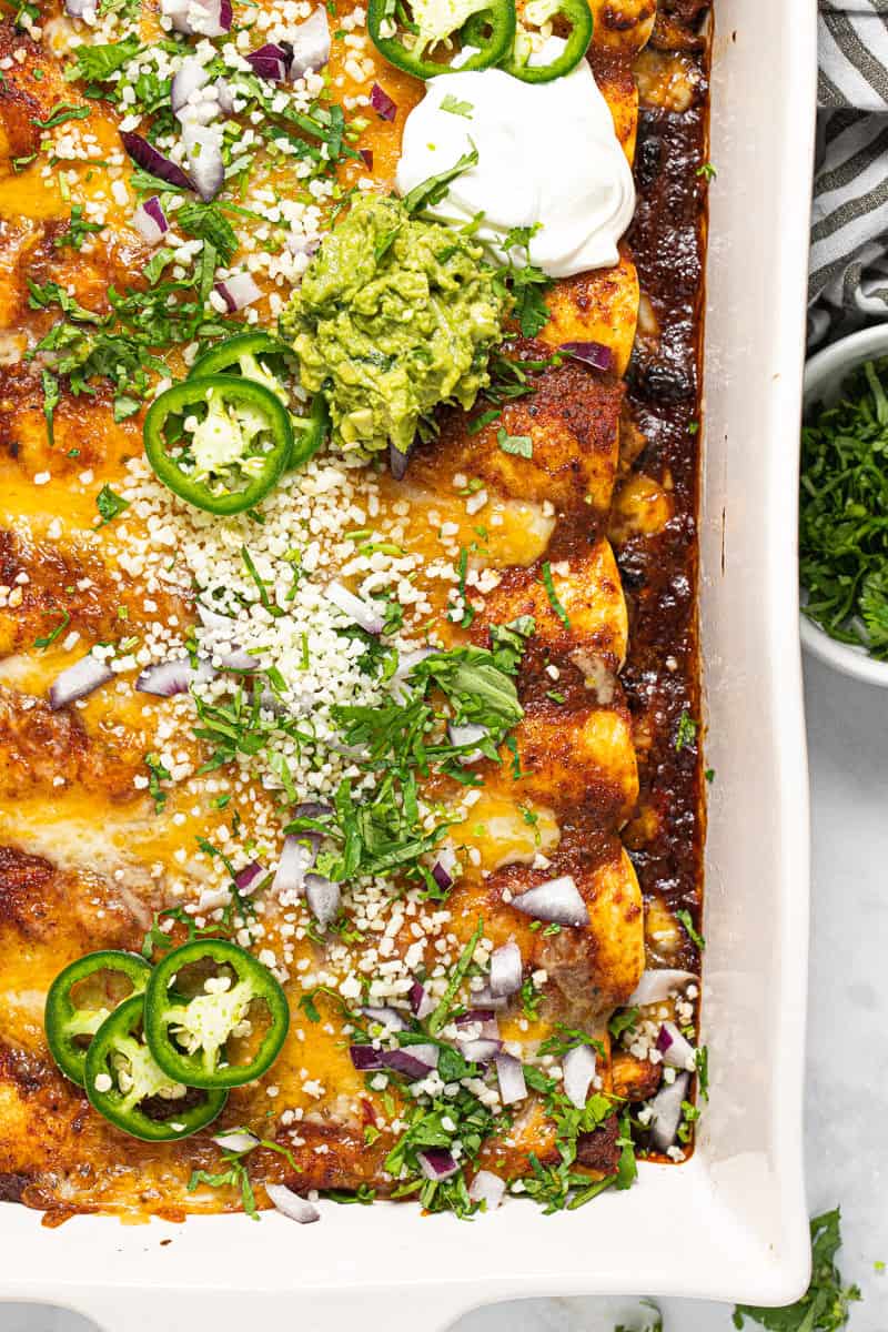 White baking dish filled with homemade cheesy chicken enchiladas garnished with fresh cilantro