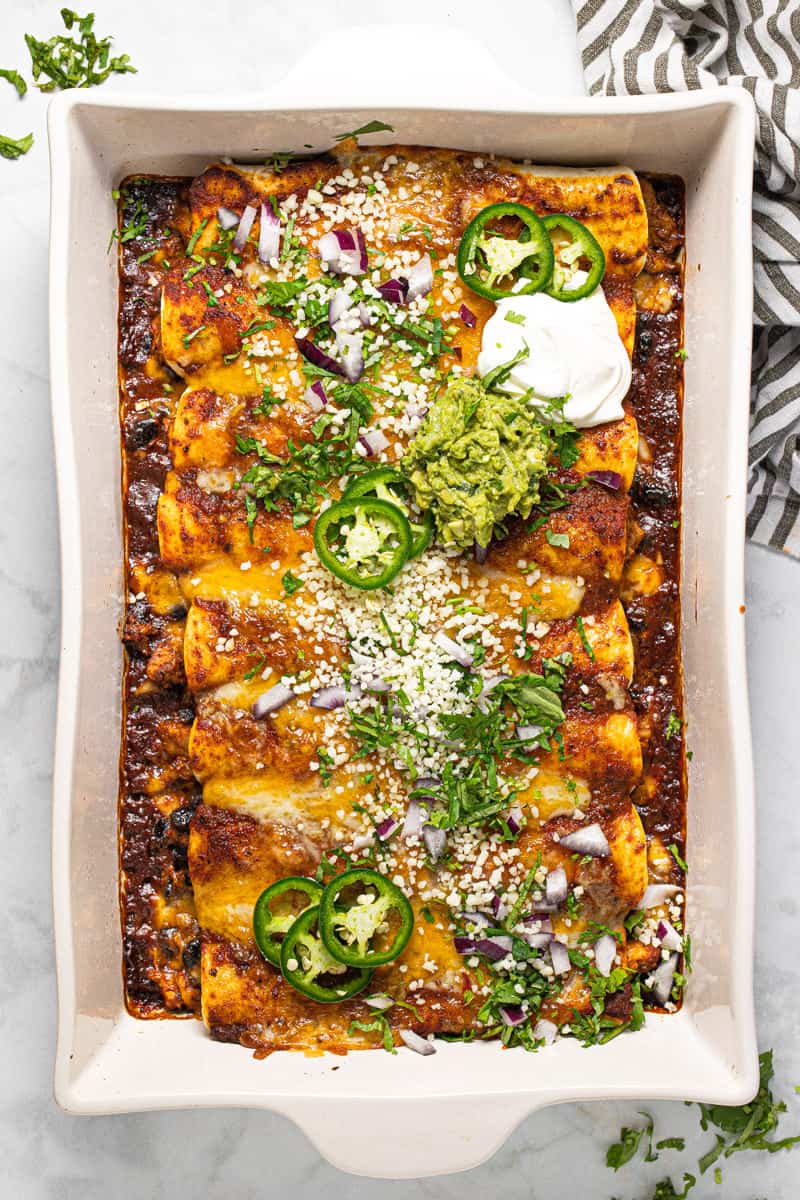 White baking dish filled with homemade cheesy chicken enchiladas garnished with fresh cilantro