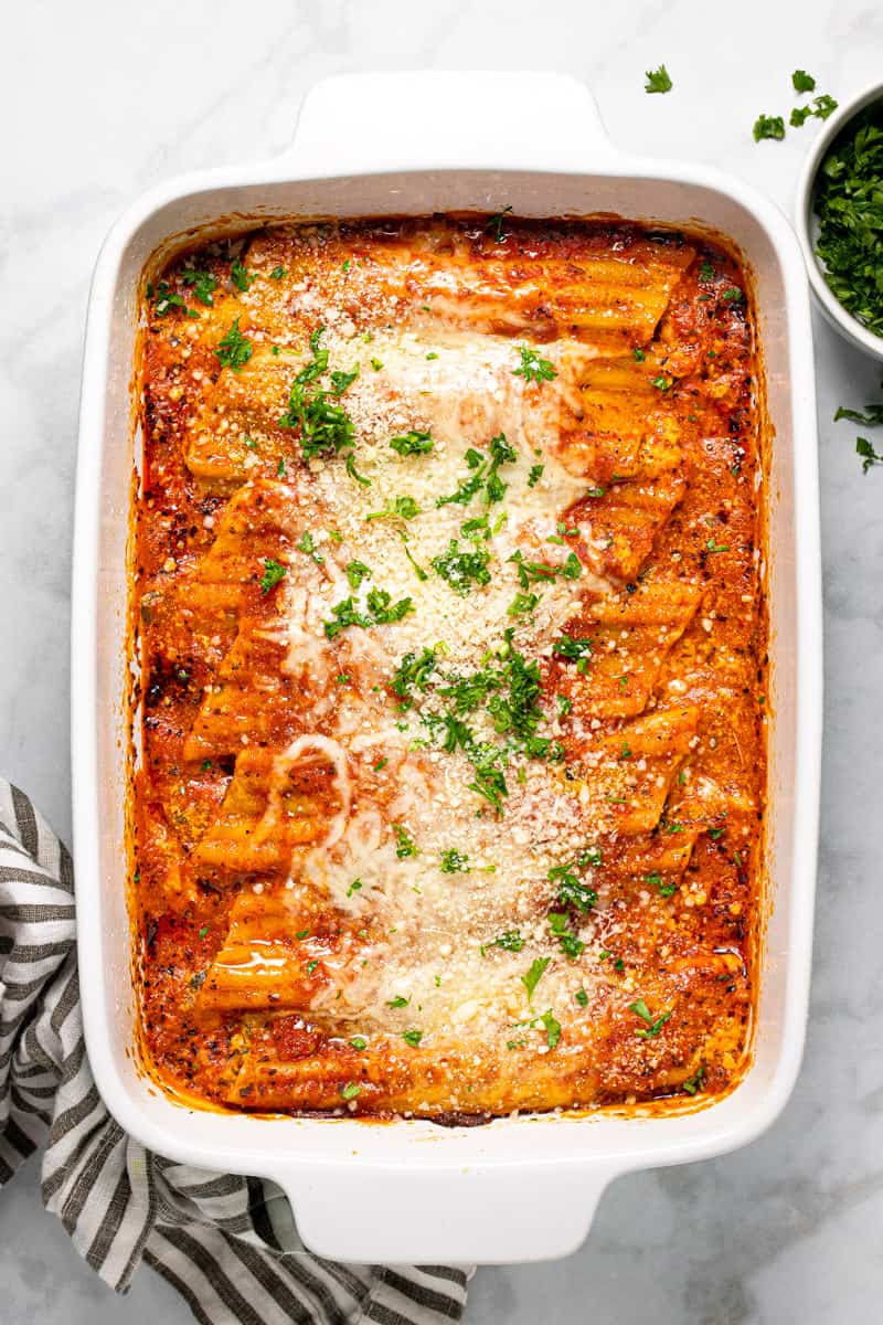 Large white baking dish filled with fresh baked homemade cheesy baked manicotti garnished with fresh parsley