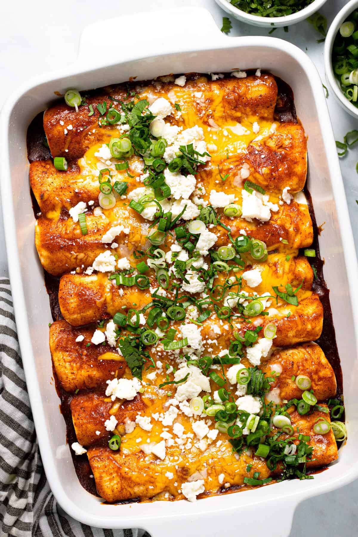 Large white baking dish filled with black bean and veggie enchiladas garnished with green onion