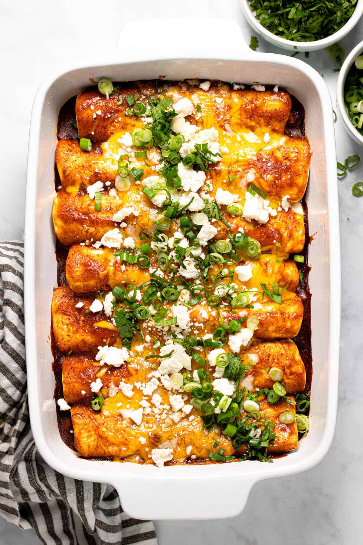 Large white baking dish filled with black bean and veggie enchiladas garnished with green onion