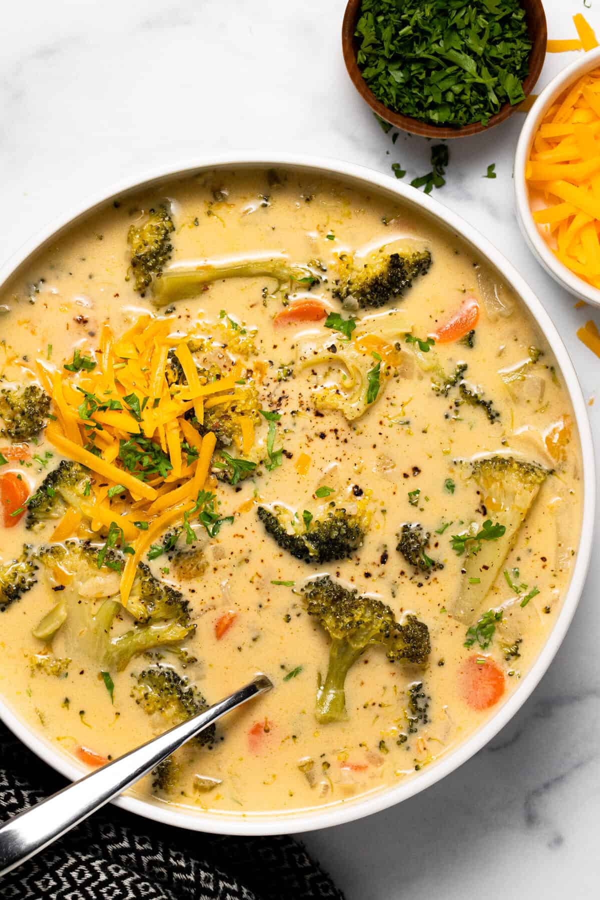 Large white bowl filled with broccoli cheddar soup topped with shredded cheese
