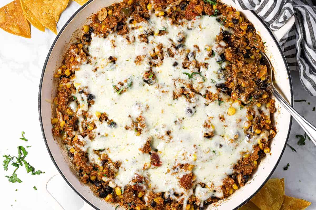 Mexican quinoa in a large white pan with melted pepper jack cheese on top