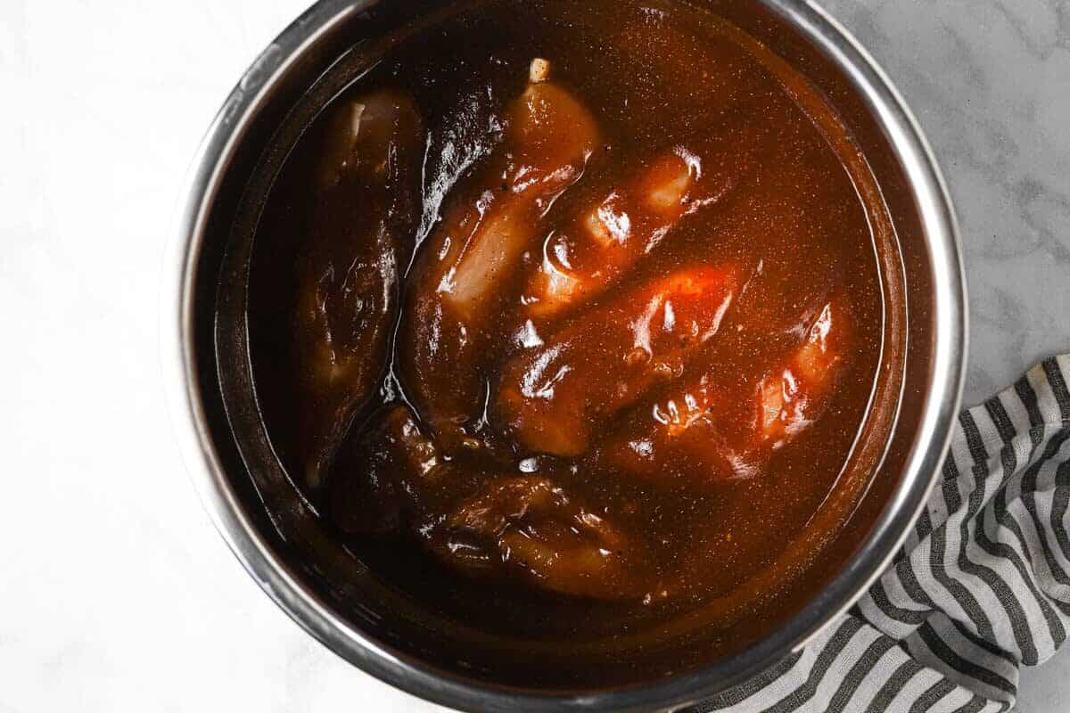 Instant pot insert with raw chicken breast and BBQ sauce in it 