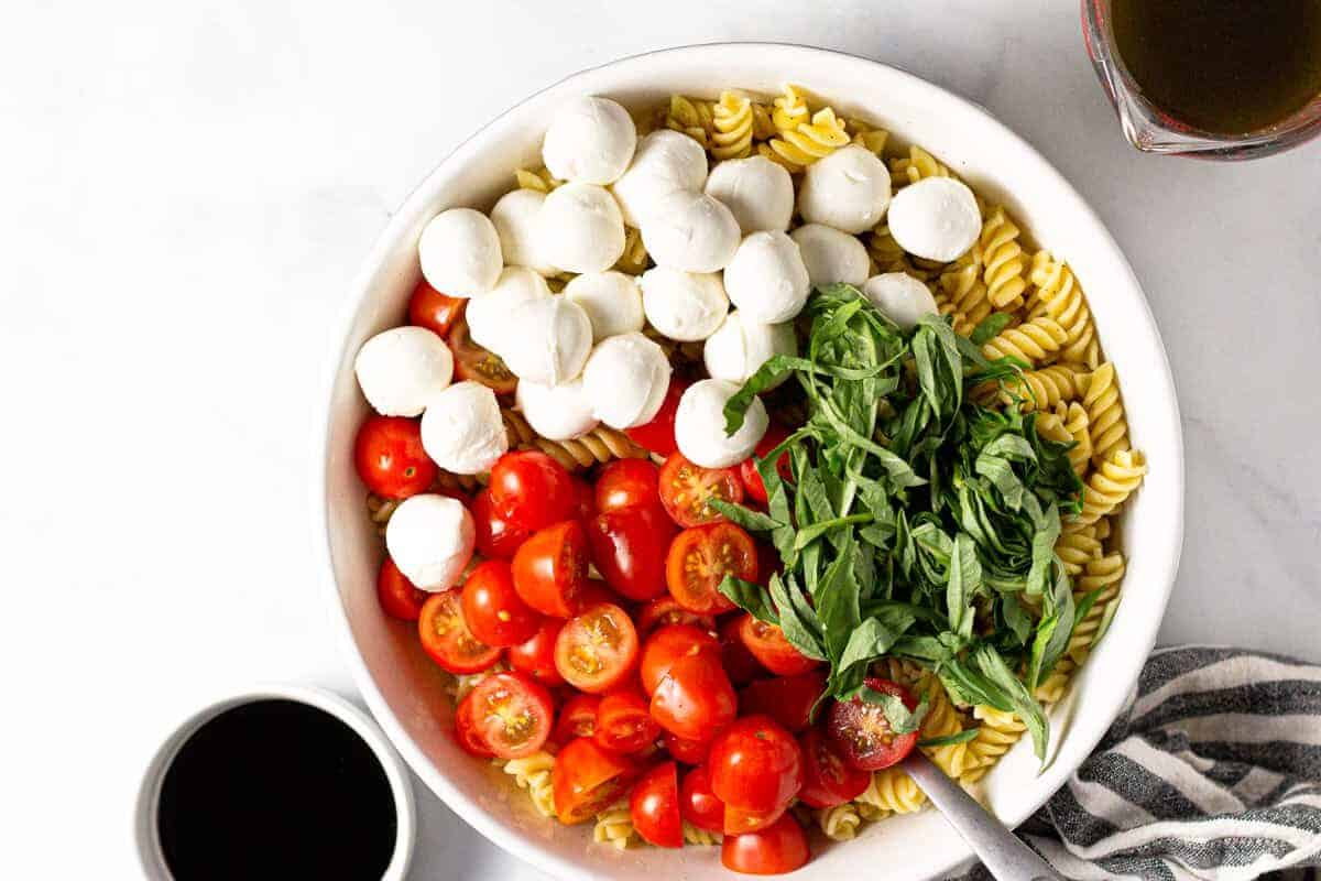 Large white bowl filled with ingredients to make a Caprese pasta salad