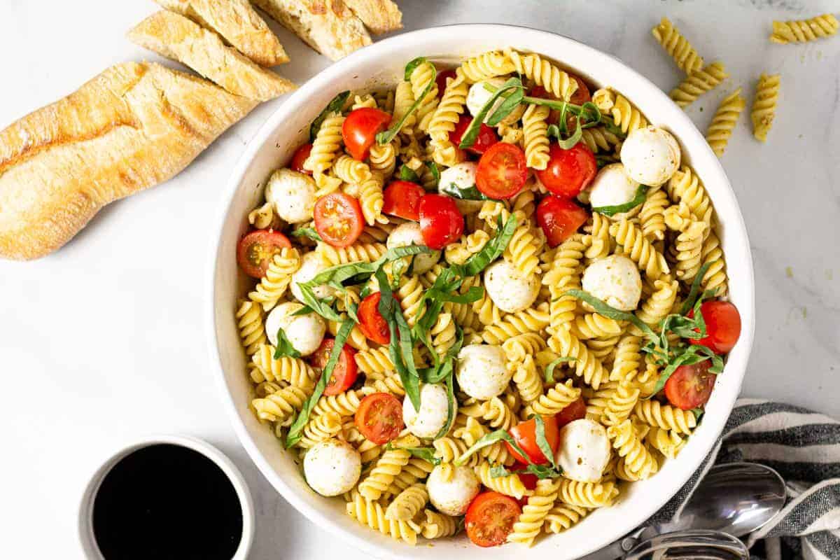 Large white bowl filled with ingredients to make a Caprese pasta salad