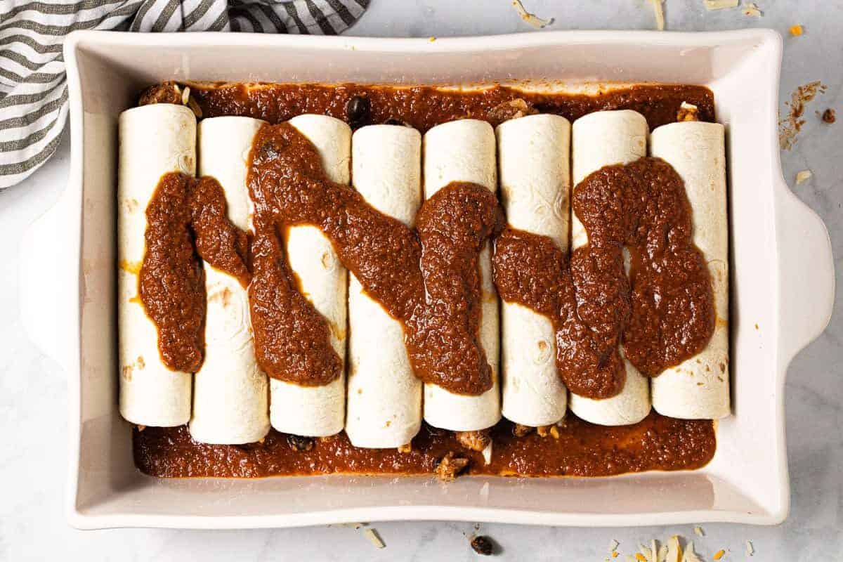 White baking dish with homemade chicken enchiladas drizzled with enchilada sauce